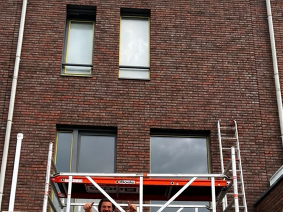 Bakstenen gevel met donkere kozijnen en een rolsteiger