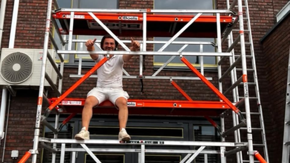 Gökhan Çevik op de rolsteiger bij een gevel met donkere kozijnen